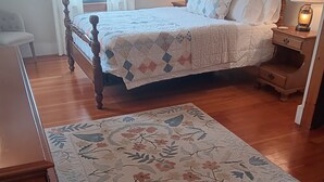 Un dormitorio con una cama de madera, una mesita de noche con lámpara, una mesita auxiliar y un tapete con motivos florales.