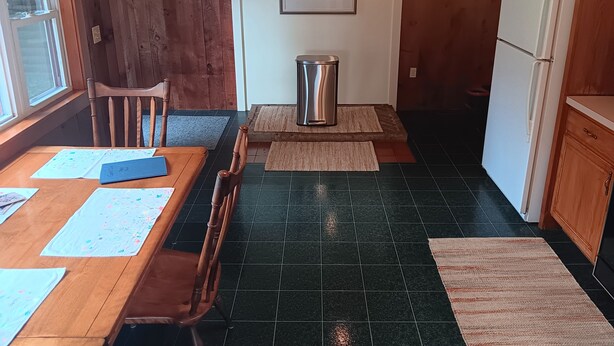 Una cocina compacta con una mesa, sillas, un cesto de basura y un refrigerador.