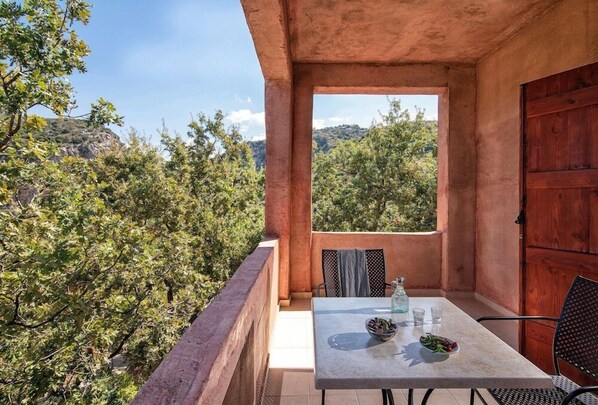 Un balcón con mesa, sillas y vistas a árboles y colinas.