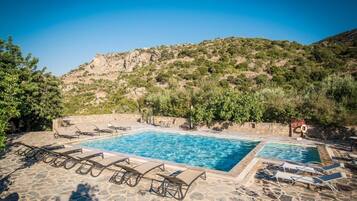 A pool area with two pools, lounge chairs, and a mountainous backdrop.
