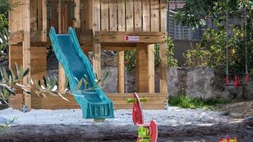 A wooden playhouse with a slide and a swing set.