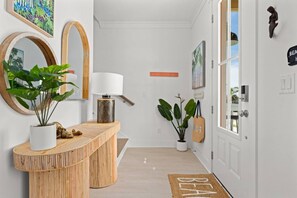 A hallway with a reception desk, potted plants, framed artwork, and a welcome mat. - Pet-Friendly Beach House with Ocean Views (Port St. Joe)