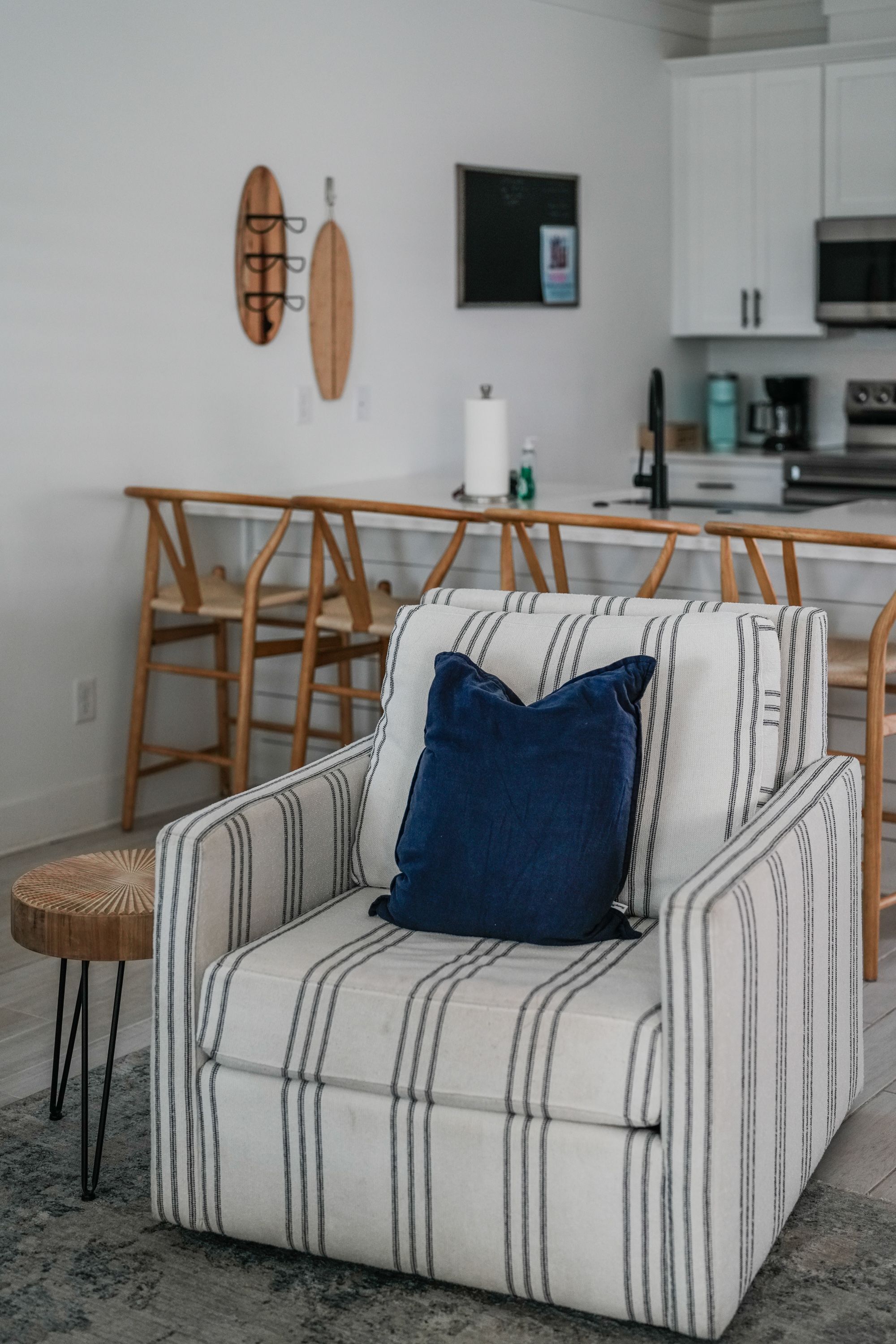 A modern living room with a striped armchair, a small round side table, and a kitchen area in the background.