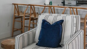 Ein modernes Wohnzimmer mit einem gestreiften Sessel, einem kleinen runden Beistelltisch und einer Küchenzeile im Hintergrund.