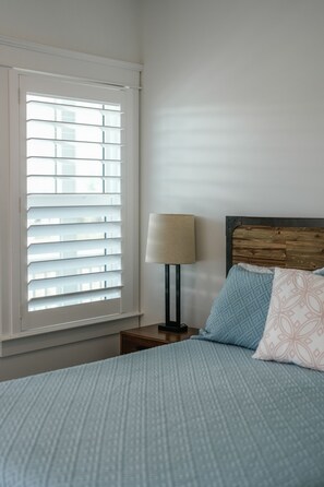 A bedroom with a bed, a nightstand, a lamp, and a window with blinds. - Pet-Friendly Beach House with Ocean Views (Port St. Joe)