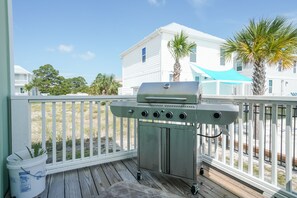 A barbecue grill on a wooden deck with a white fence, a white house, and palm trees in the background. - Pet-Friendly Beach House with Ocean Views (Port St. Joe)