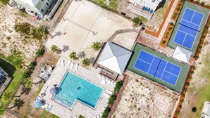 Luftaufnahme eines Resorts mit Schwimmbad, Tennisplätzen und einer überdachten Liegefläche.