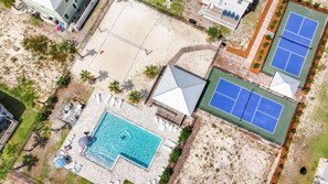 Luftaufnahme eines Resorts mit Schwimmbad, Tennisplätzen und einer überdachten Liegefläche.