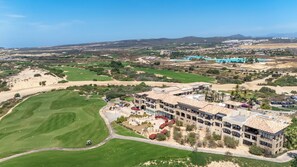 A golf course with a building featuring multiple balconies and a view of the surrounding landscape. - Beachfront 2BR Condo with Hot Tub at Diamante Dunes (Cabo San Lucas)