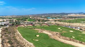 Ein Golfplatz mit Bunkern, einem Clubhaus und Wohnhäusern im Hintergrund.