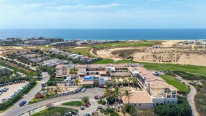 A resort with multiple buildings, a parking area, and a view of the beach and ocean. - Beachfront 2BR Condo with Hot Tub at Diamante Dunes (Cabo San Lucas)