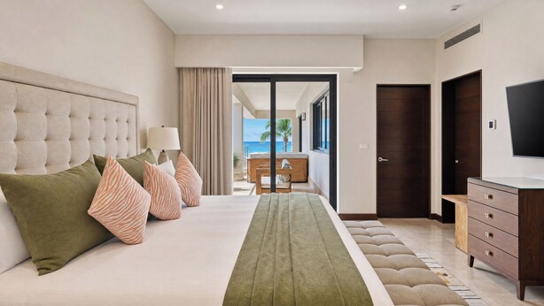 A hotel room with a bed, a TV, a dresser, and a view of the ocean. - Beachfront 2BR Condo with Hot Tub at Diamante Dunes (Cabo San Lucas)