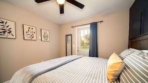 Une chambre à coucher comprenant un lit, un ventilateur de plafond, une porte et deux tableaux accrochés au mur.