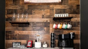 Un coin café avec un mur en bois rustique, une machine à café, des tasses et divers accessoires pour préparer le café.