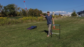 Une personne se tient dans un champ d’herbe, près d’une structure d’escalade bleue et rouge et d’un ballon rouge.