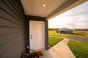 A house with a white door, a porch, and a view of a building across a grassy field. - Last Light | Wine Cellar | Wine Trail | Firepit (Lodi)