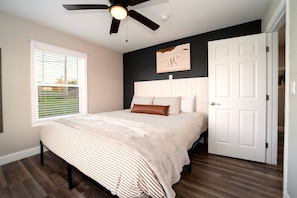 A bedroom with a bed, a ceiling fan, a window with blinds, and a door. - Last Light | Wine Cellar | Wine Trail | Firepit (Lodi)
