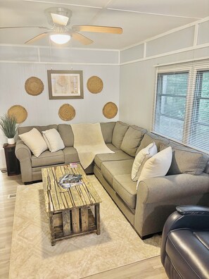 A living room with a sectional sofa, a wooden coffee table, a ceiling fan, and decorative wall hangings. - Relaxing lake front property with kayak/paddleboard. (Martin)