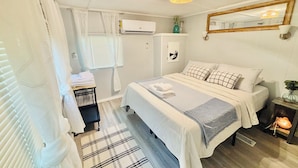 A bedroom with a bed, a bedside table, a mirror, a window with blinds, an air conditioning unit, and a ceiling light fixture. - Relaxing lake front property with kayak/paddleboard. (Martin)