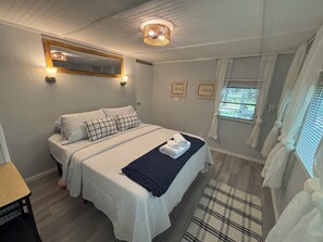 Een slaapkamer met een bed, bedlampen, een spiegel en een raam met gordijnen.