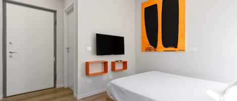 A bedroom with a bed, a television mounted on the wall, and a door.