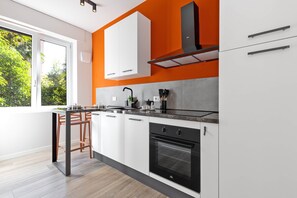 A modern kitchen with white cabinets, a black oven, and a window overlooking greenery. - The Cheerful Two-Room Apartment "L'Arancio" in Central Bergamo (Bergamo)