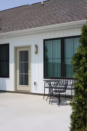A building with a white exterior, a large window, and a door. There is a small outdoor seating area with a table and chairs. - Studio in Sugarcreek Steps away from Spa and Café (Sugarcreek)