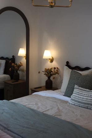 A neatly made bed with a headboard, a bedside table with a lamp and a vase of flowers, and a large mirror on the wall. - Studio in Sugarcreek Steps away from Spa and Café (Sugarcreek)