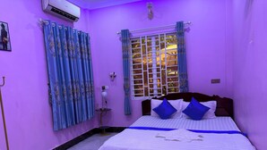 A bedroom with a bed, curtains, a window, and a wall-mounted air conditioner. - Bun homestay  (Battambang)