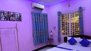 A room with a bed, a window with curtains, a wall-mounted air conditioner, and a drying rack. - Bun homestay  (Battambang)
