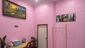 A room with pink walls, a wooden desk with a chair, a framed landscape painting, a coat rack, and a door. - Bun homestay  (Battambang)