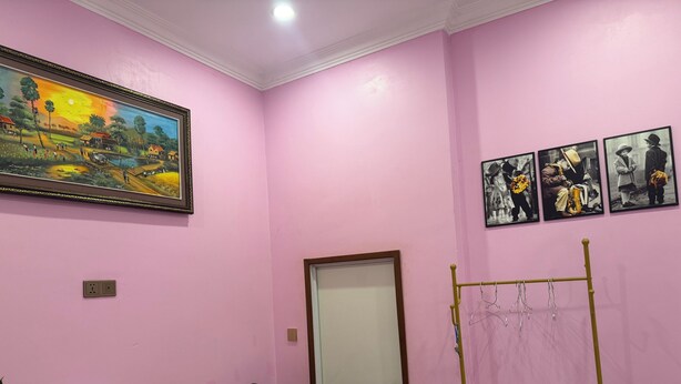 A room with pink walls, a wooden table, a chair, a door, and a coat rack. - Bun homestay  (Battambang)