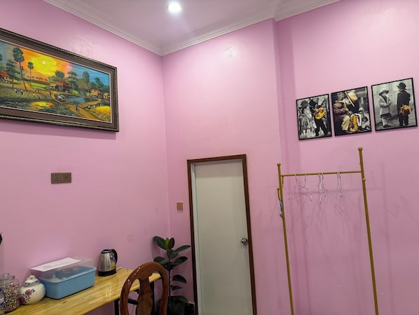 A room with pink walls, a wooden table, a chair, a door, and a coat rack.