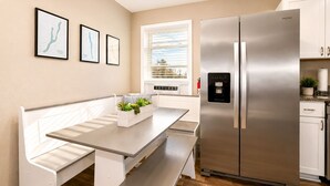 Une cuisine moderne avec un réfrigérateur en acier inoxydable, un banc en bois et une fenêtre équipée de stores.