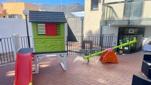 Un área de juegos infantiles con un tobogán, una estructura para escalar y un balancín.