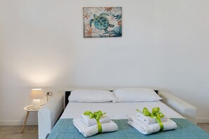 A hotel room with a bed, two pillows, a nightstand with a lamp, and two towels with green ribbons.