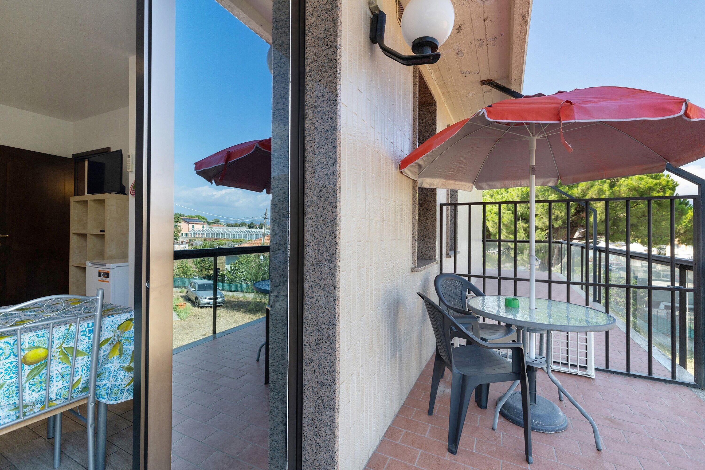 Un balcon avec une table et des chaises, un parasol rouge et une vue sur le quartier.