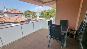 En balkon med et bord og stole, udsigt til bygninger og træer, og et flisegulv.