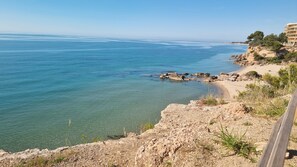 Eine Küstenlandschaft mit freiem Blick auf das Meer, felsigem Gelände und einem Gebäude mit mehreren Balkonen.