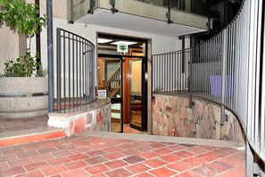 A hotel entrance with a stone wall, metal railing, and a staircase leading inside.