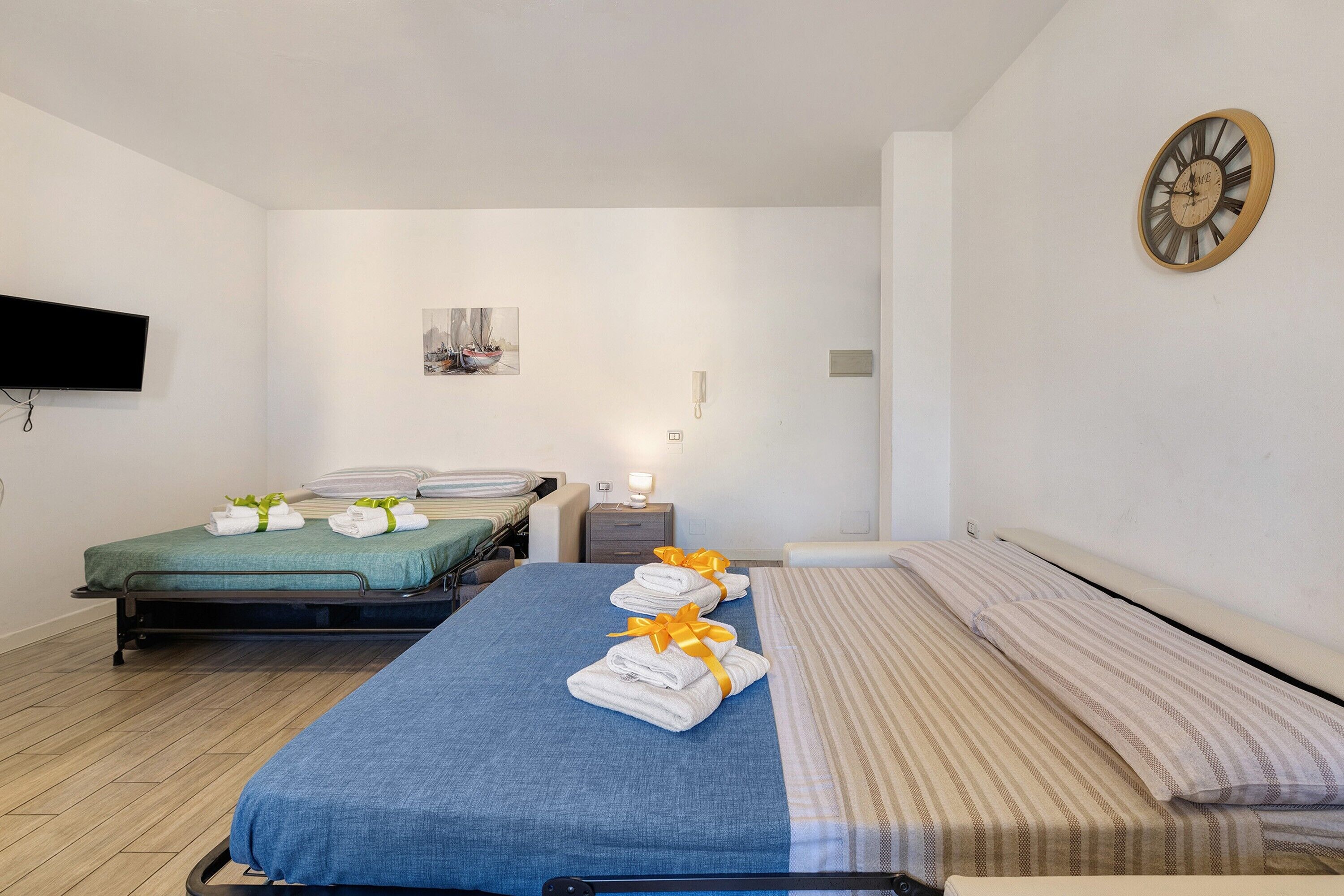 Une chambre d’hôtel avec deux lits, un téléviseur à écran plat, un tableau, un téléphone et une horloge murale.