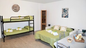 Una stanza con letti a castello, un comodino, una lampada, una sveglia, uno scaffale con stoviglie e un quadro.