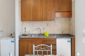 A kitchen with wooden cabinets, a granite countertop, a sink, and a small refrigerator.