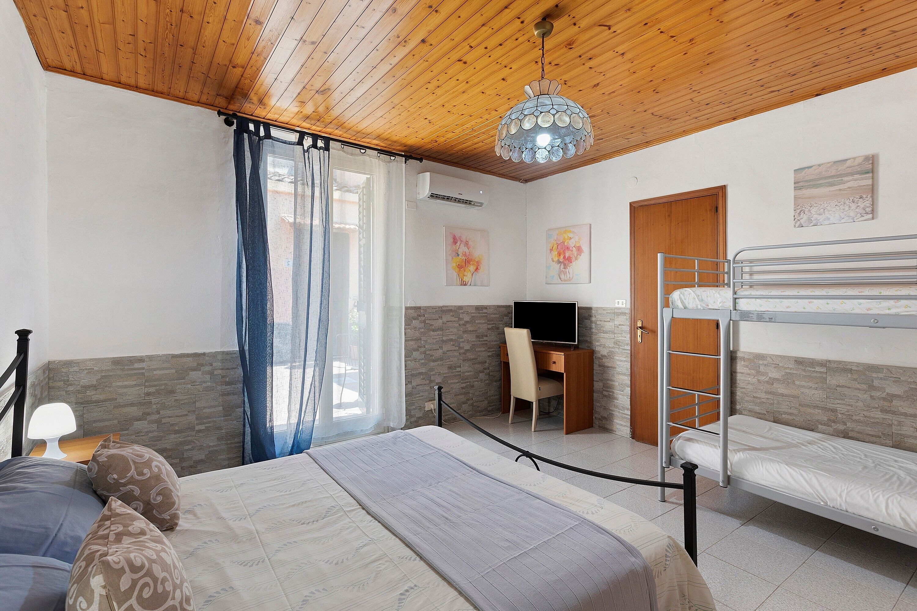 Ein Zimmer mit einem Etagenbett, einem Schreibtisch mit Stuhl, einem Fernseher und Bildern an den Wänden.