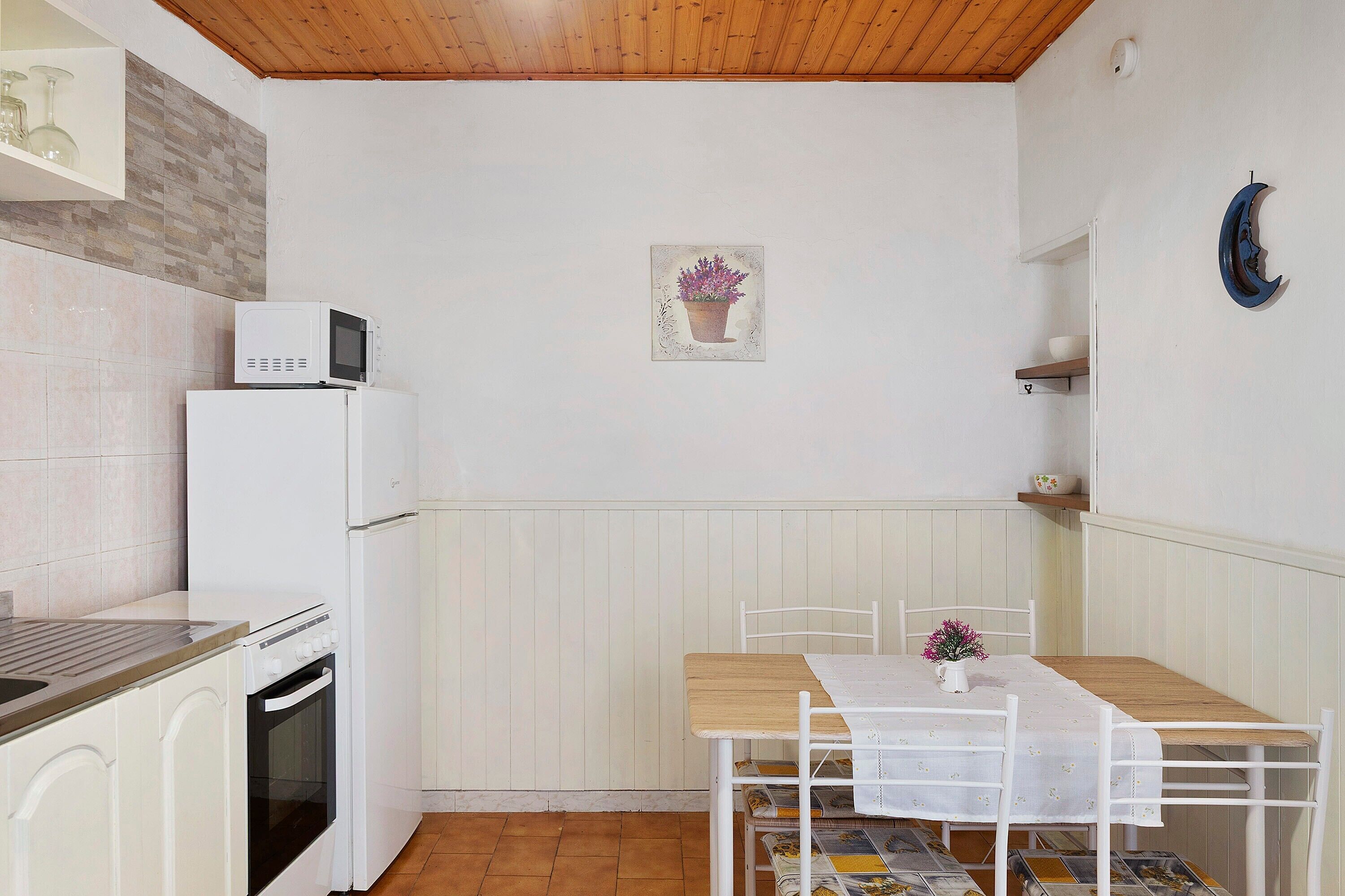 Una cucina compatta con forno a microonde, frigorifero, forno e un tavolo con sedie.