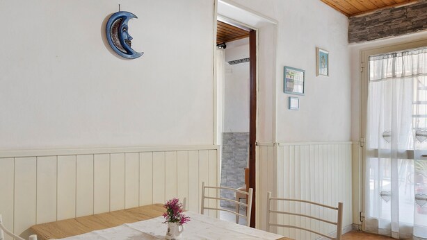 Un coin repas avec une table en bois, des chaises blanches, une nappe blanche et un vase rempli de fleurs roses.