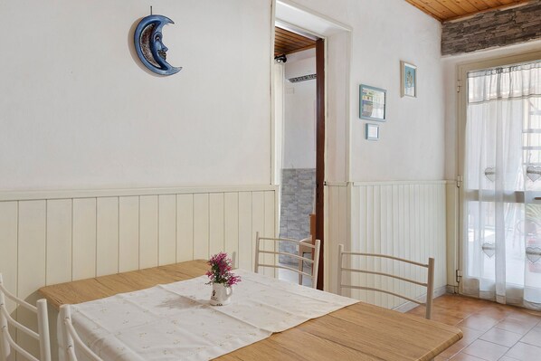 Un coin repas avec une table en bois, des chaises blanches, une nappe blanche et un vase rempli de fleurs roses.