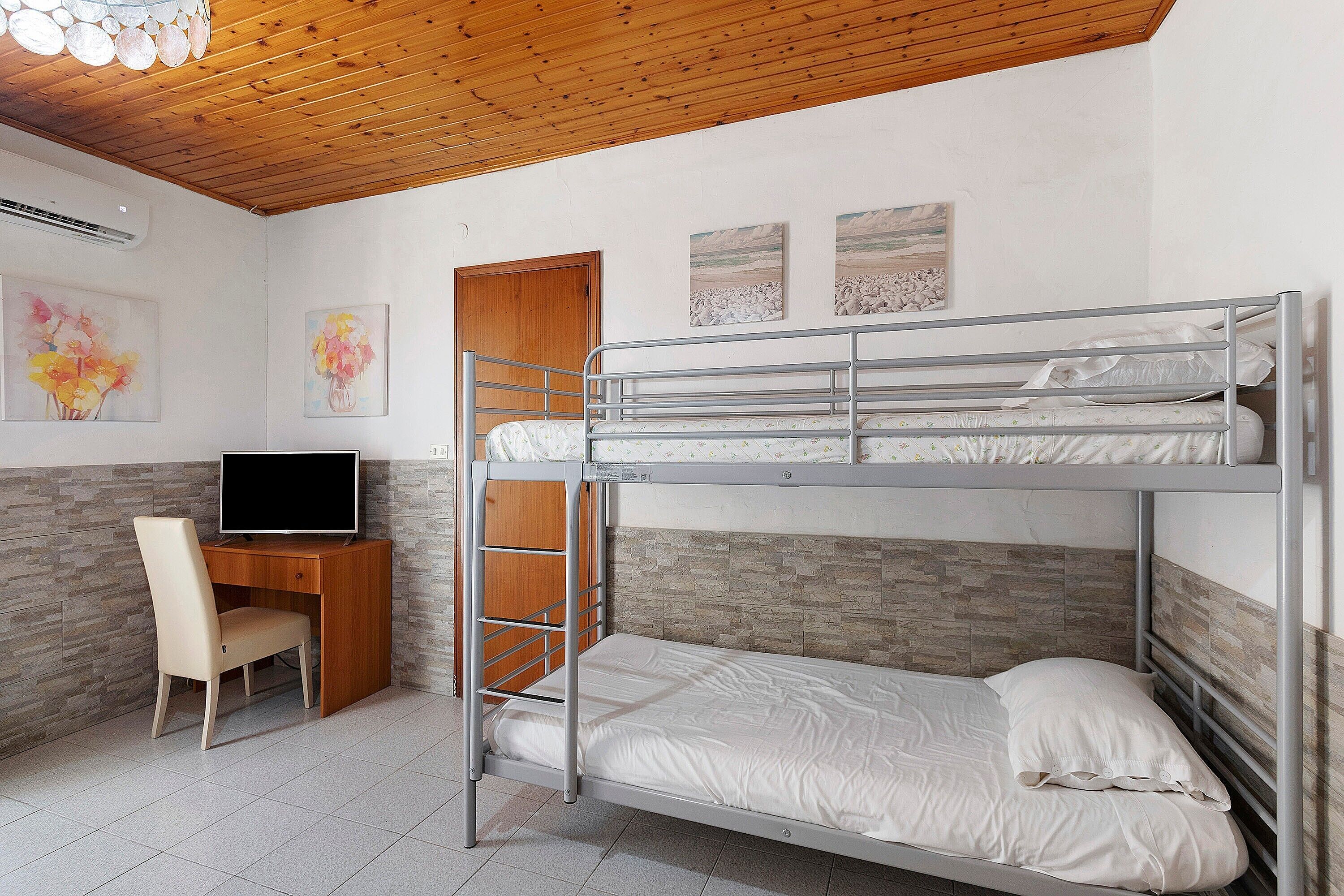 Una stanza con letto a castello, una scrivania e una sedia, televisione e opere d'arte alle pareti.