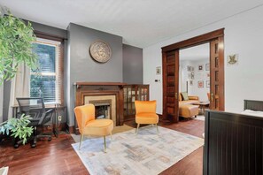 A living room with a fireplace, two armchairs, a desk, and a bookshelf. - 1918 Charm Meets Modern  OSU-Close Gem (Columbus)