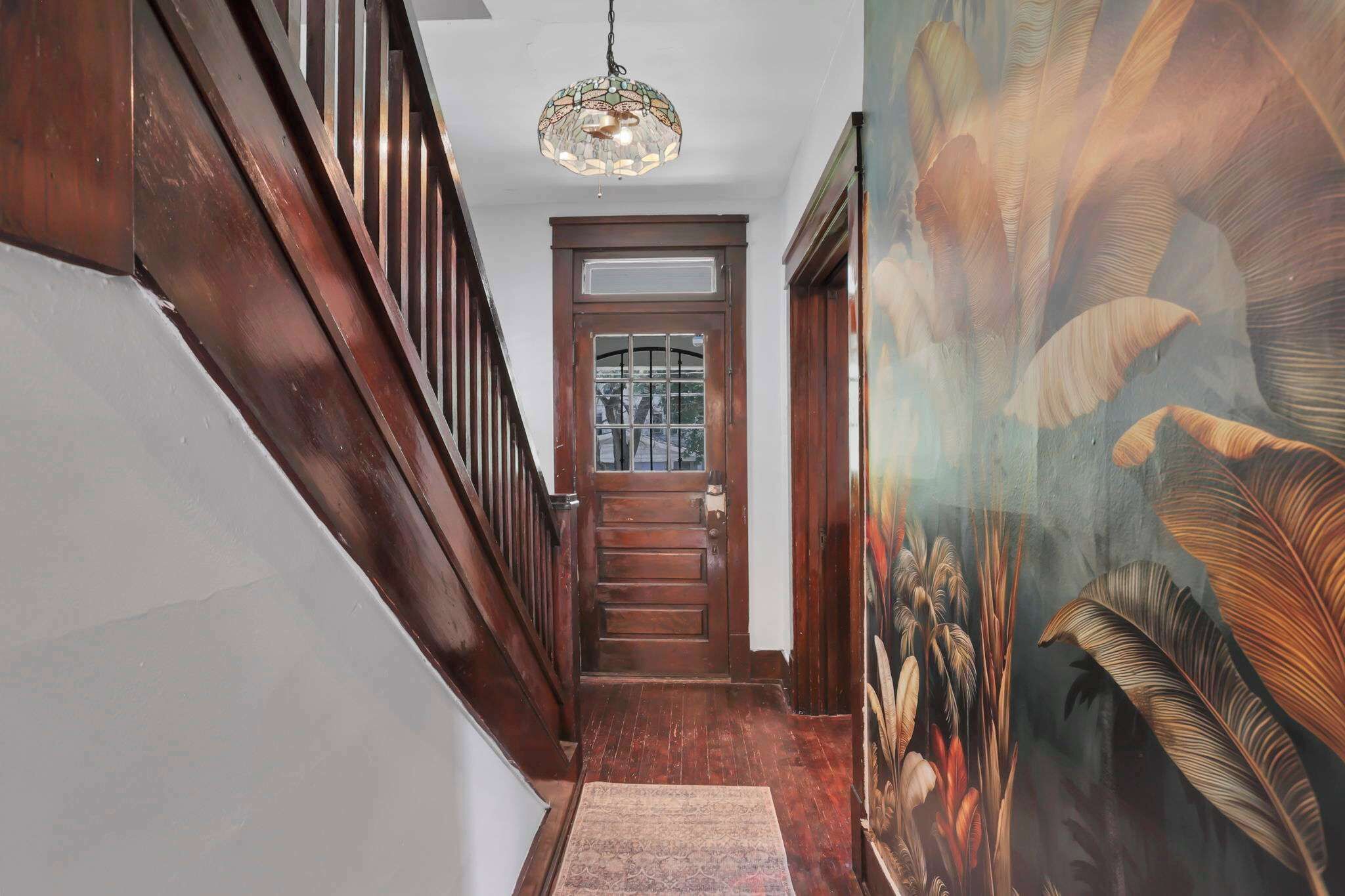 A wooden staircase with a glass door at the top, a patterned wall, and a hanging light fixture.